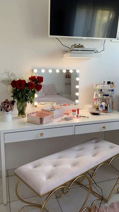 a vanity table with a mirror, stool and flowers on it in front of a flat screen tv