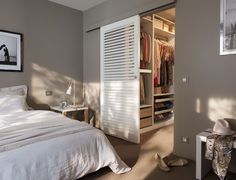 a bedroom with an open closet door and white bed in the corner, next to a dresser