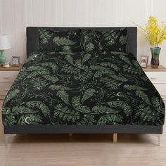 a bed with a black and green comforter on top of it next to a night stand