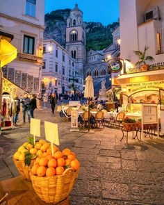 a basket full of oranges sitting on top of a wooden table in front of a building