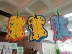 three clocks are hanging from the ceiling in an art room with children's drawings on them