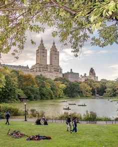 people are walking around in the park by the water and buildings on the other side