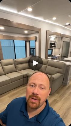 a man standing in front of a living room with a couch and kitchen behind him