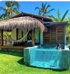 a woman sitting in the middle of a pool next to a hut with thatched roof