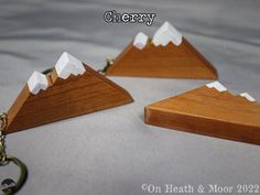 three pieces of wood with white mountains on them and a keychain attached to it