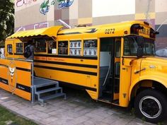 a yellow school bus parked in front of a building with its doors open and people standing outside