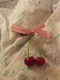 two cherries tied to a pink ribbon on top of a white sheet with flowers