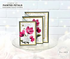 two cards with pink flowers on them sitting on a glass plate next to a white brick wall