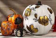 three painted pumpkins sitting next to each other on a wooden surface with leaves and flowers