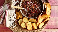 a bowl filled with chili and crackers on top of a wooden table next to a napkin