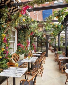 an outdoor dining area with wicker chairs and tables covered in hanging plants, surrounded by potted greenery