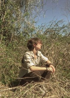 a young man sitting on the ground in tall grass