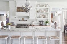 a white kitchen with lots of counter space and stools in front of the island