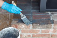 a person in blue gloves is painting a brick wall