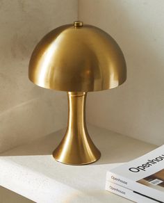 a gold lamp sitting on top of a white shelf next to a book and magazine