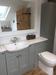 a white toilet sitting under a bathroom mirror next to a sink in a room with wooden floors