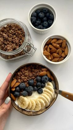 a person is holding a spoon over a bowl of cereal and bananas with blueberries