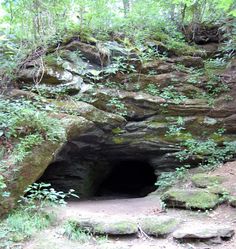 a cave in the side of a mountain with moss growing on it's sides