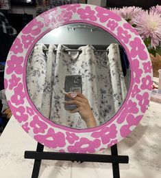 a pink and white flowered mirror on a table with flowers in the background,