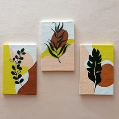 three square paintings with leaves on them are hanging on the side of a white wall