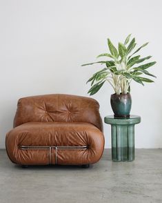 a brown leather chair next to a green table with a potted plant on it