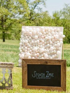 a blackboard with white balls on it next to a wooden sign that says, 28 guests throw darts at balloons filled with paint attached to a canvas you keep the art