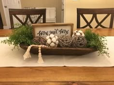 a wooden tray filled with balls and greenery on top of a dining room table