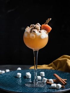 an orange drink with marshmallows and cinnamon on a blue plate next to a yellow napkin