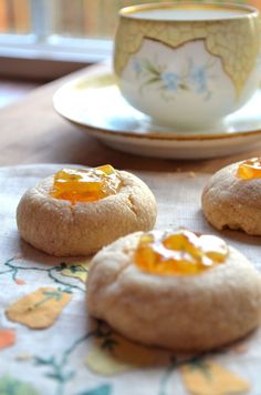 three cookies are sitting on a table next to a cup and saucer with orange marmalade toppings