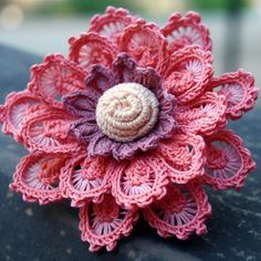 a crocheted pink and purple flower with a shell in the center sits on a black surface