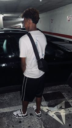 a young man standing in front of a black car with his back to the camera