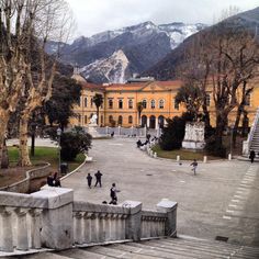 people are walking around in front of a large building with mountains in the back ground