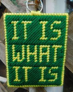 a green and yellow knitted sign hanging from a wooden pole with a keychain