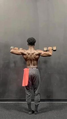 a man standing in front of a mirror with his back turned to the camera and holding two dumbbells