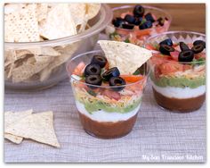 three cups filled with different types of dips and tortilla chips on top of a table