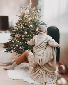 a woman sitting on the floor next to a christmas tree