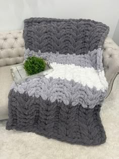 a gray and white blanket sitting on top of a couch next to a green plant