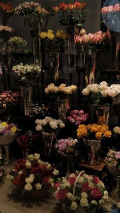 a bunch of flowers that are in vases on a table and some people looking at them