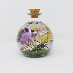 a glass bottle filled with flowers on top of a white table next to a cork lid