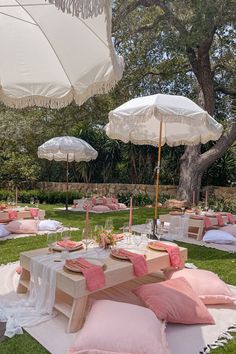 an outdoor picnic setting with white umbrellas and pink pillows