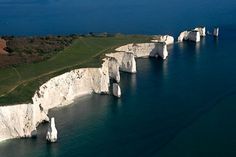 an aerial view of white cliffs in the ocean with green grass and blue water around them