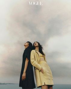 two women standing next to each other in front of the ocean with their eyes closed