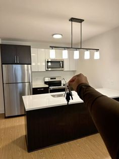 a person holding a house key in front of an open kitchen with stainless steel appliances