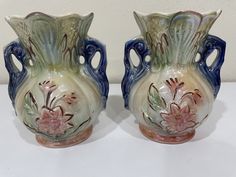 Enhance your home decor with this elegant pair of Lusterware Opalescent Iridescent Ceramic Bud Vases with Handles. These unique vases, made in Brazil, are crafted from high-quality ceramic material and feature an iridescent finish that sparkles in the light. Measuring 5 inches in height and 4 inches in width, these vases are perfect for displaying your favorite flowers and adding a touch of sophistication to any room. Whether placed on a mantel, bookshelf, or centerpiece, these vases are sure to be a standout piece. The handles add a charming touch to the design, making these vases not only stylish but also functional. Don't miss out on the opportunity to elevate your home decor with this beautiful set of vases. Vases With Handles, Iridescent Ceramic, Mantel Bookshelf, Ceramic Bud Vases, Unique Vases, Favorite Flowers, Bud Vase, Made In Brazil, Ceramic Materials