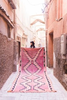 a pink and black rug sitting on the side of an alleyway in a city