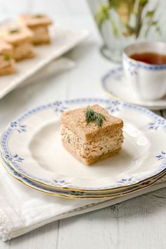 a small piece of food on a plate next to a cup of tea and cookies