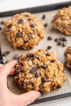 a person picking up an oatmeal chocolate chip cookie from a baking sheet