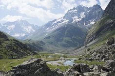 the mountains are covered in snow and green grass, with a small stream running between them