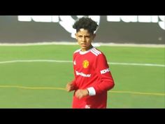 a young man standing on top of a soccer field wearing a red shirt and black pants