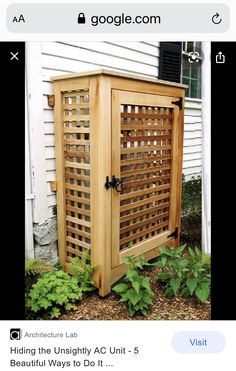 a wooden cabinet sitting in front of a house next to some plants and flowers on the ground